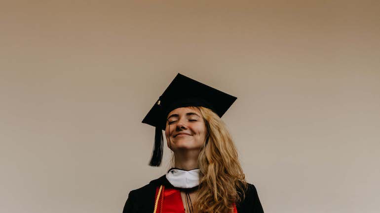 Girl against plain wall in full graduation attire