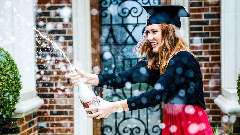 Woman in red dress and graduation cap spraying champagne