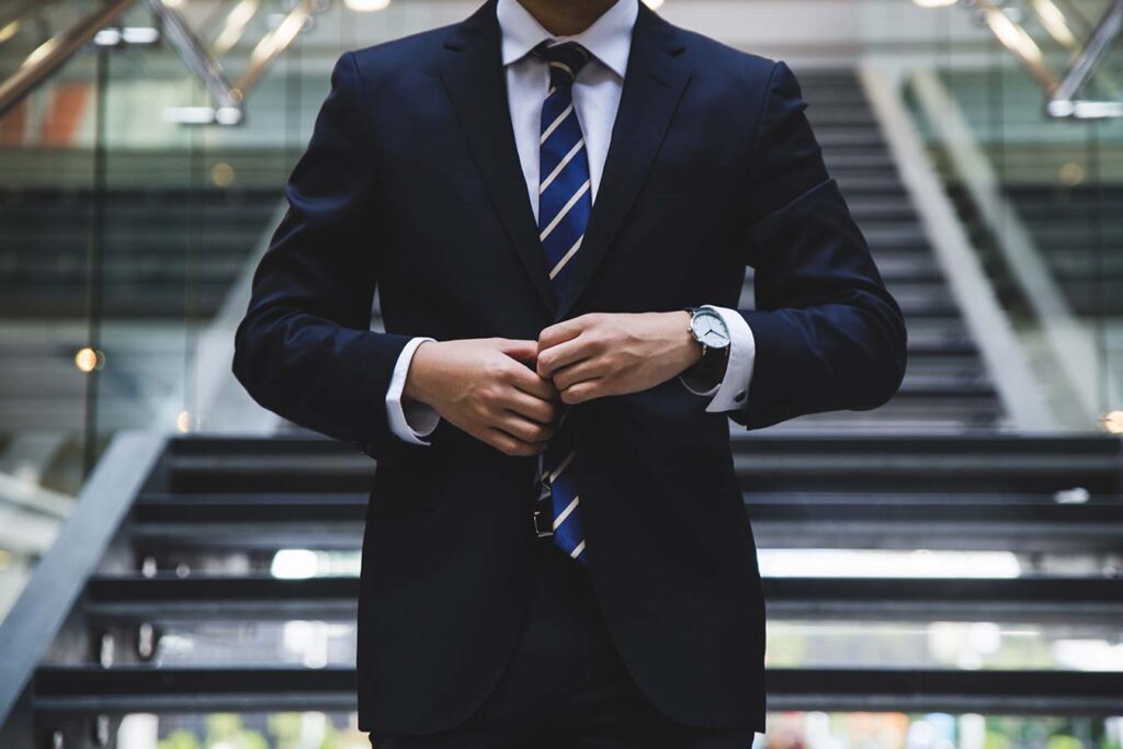 man dressed in a suit with a watch on his right hand and stairs behind him