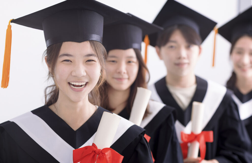 Smiling asian girl student graduate and classmates standing with diplomas in hands