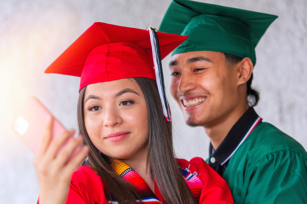 Smiling hispanic students posing the day of their graduation looking at the smart phone camera