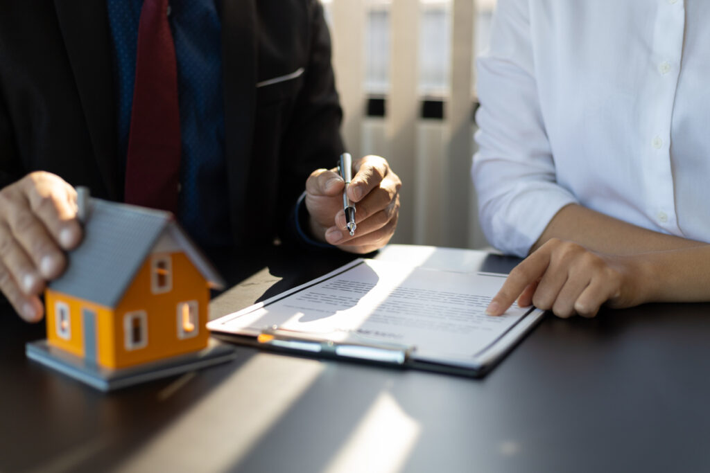 Businessman in suit in his office showing home insurance policy and pointing with a pen where the policyholder must to sign. Insurance agent consulting real estate insurance detail to customer.