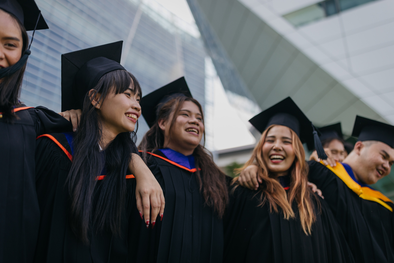 Smiling university students wearing graduation gowns are celebrating graduation in front of the university.