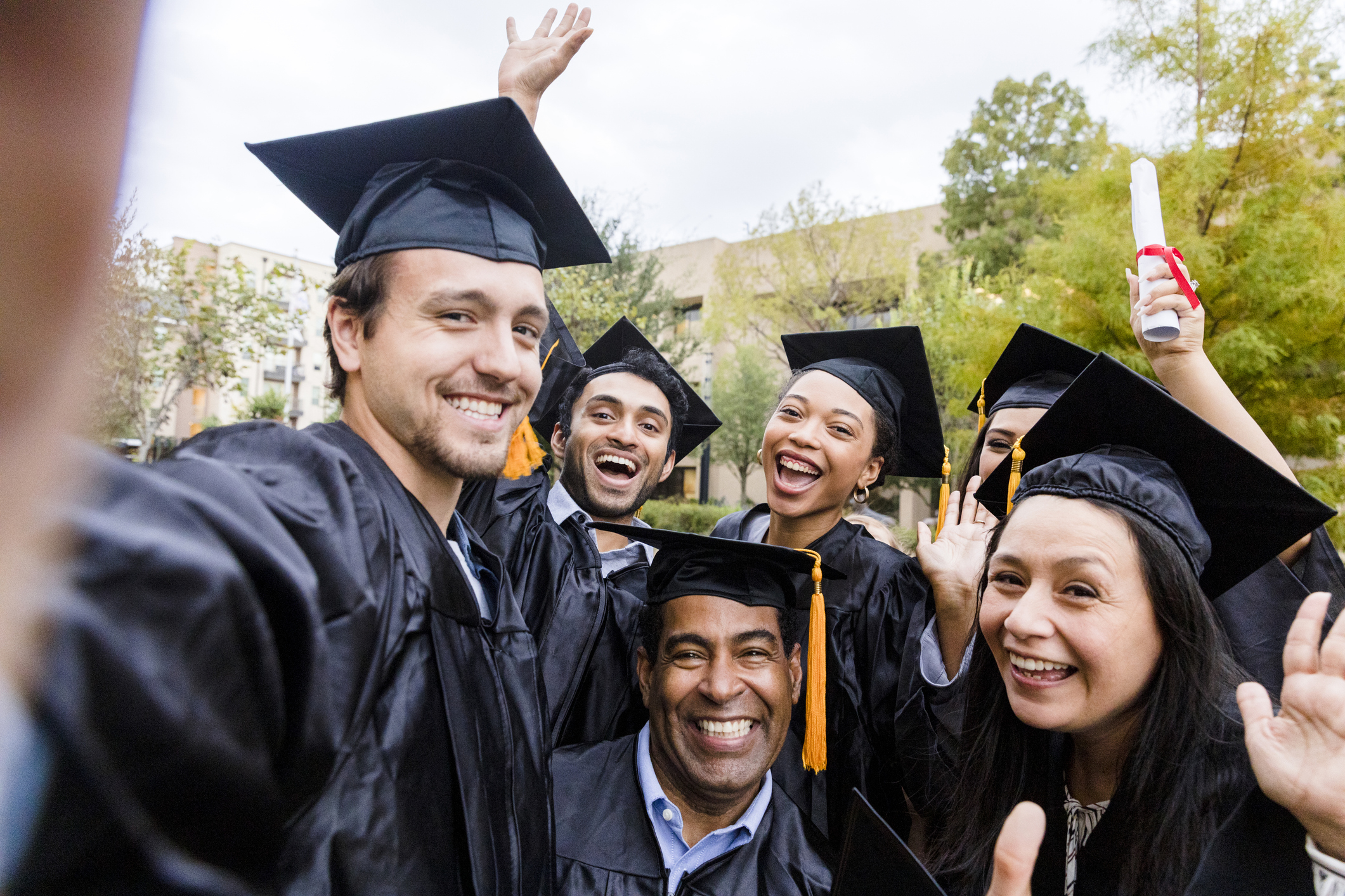 The diverse group of friends takes a selfie as they smile and cheer after the graduation ceremony.