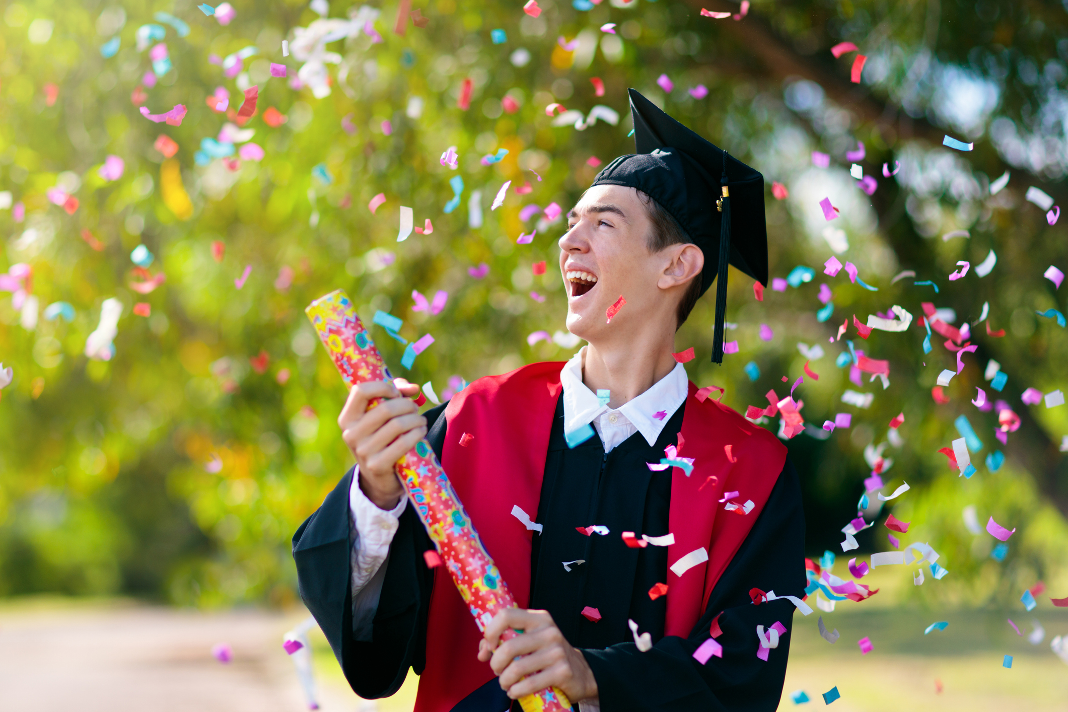 School or college graduation ceremony. Young man in academic regalia, gown and cap, celebration successful diploma certificate. High school graduate in robe, stole and mortar board.