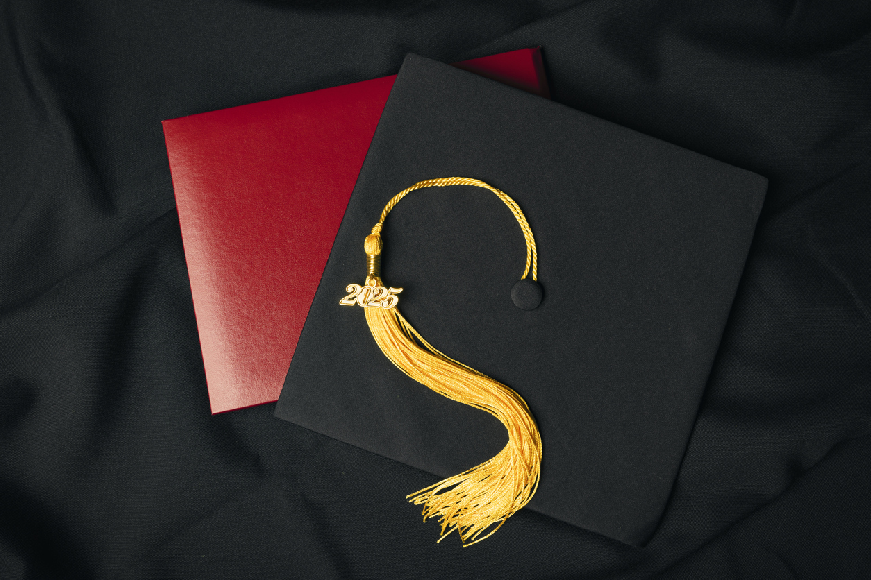A overhead view of a graduation cap and diploma with a 2025 charm on a yellow tassel.
