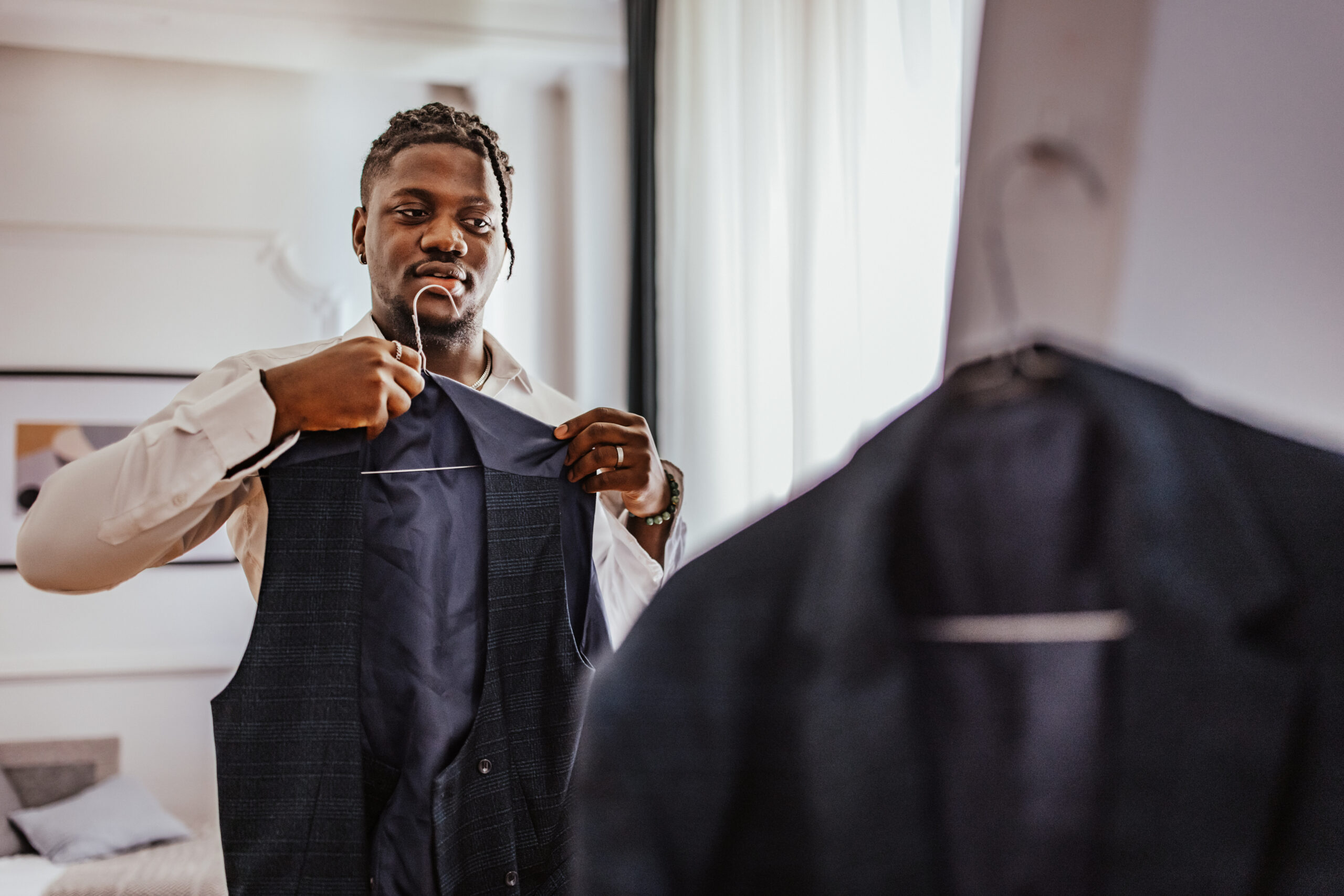 Young black man putting on a formal wear for his prom night, looking at himself in the mirror and adjusting his suit